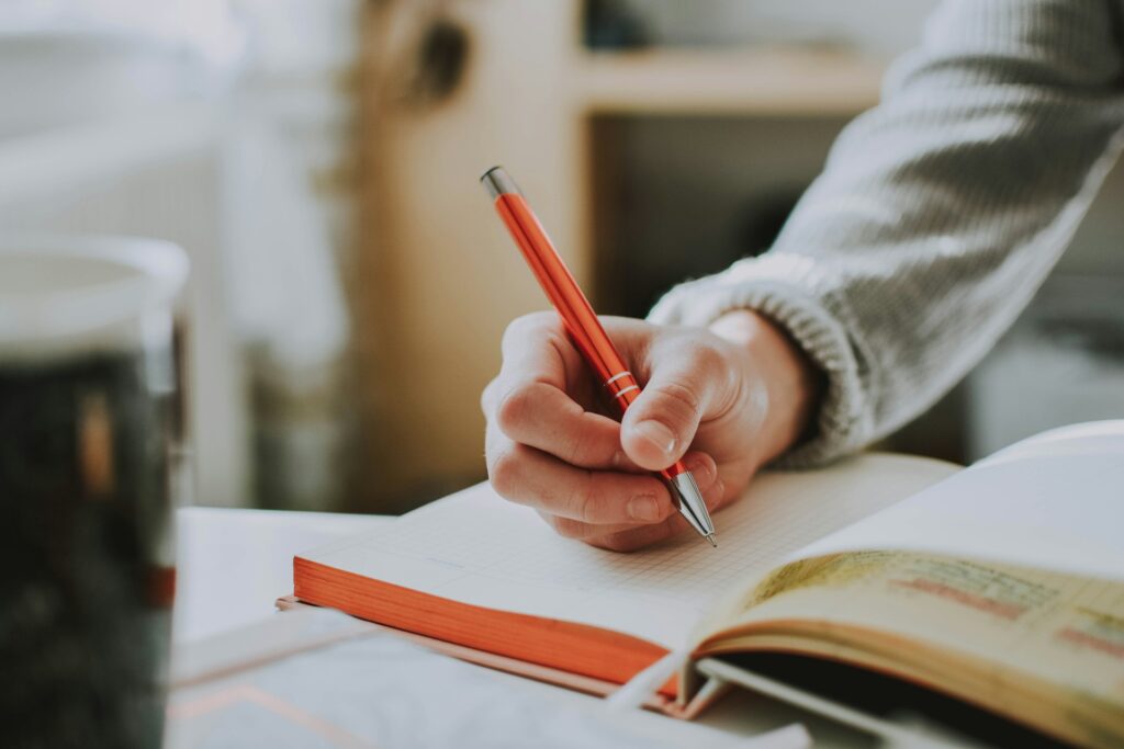 Person holding red pen while writing on notebook.